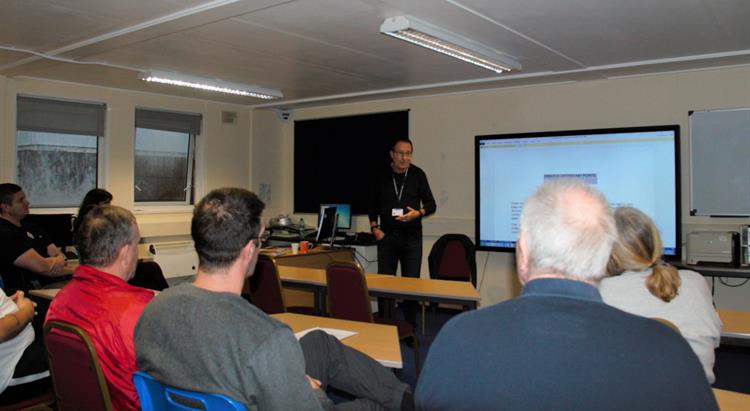 Local author Peter James speaks to prisoners while standing in front of a projector